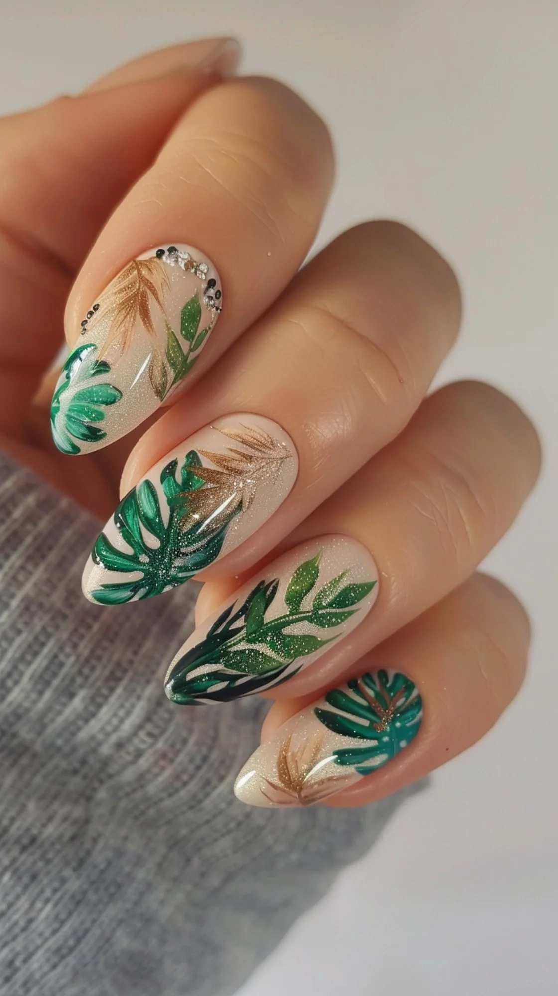 Elegant boho nails with a shimmering nude base featuring green tropical leaves and golden botanical accents. Each leaf is detailed with fine glitter lines, adding a touch of sophisticated sparkle.