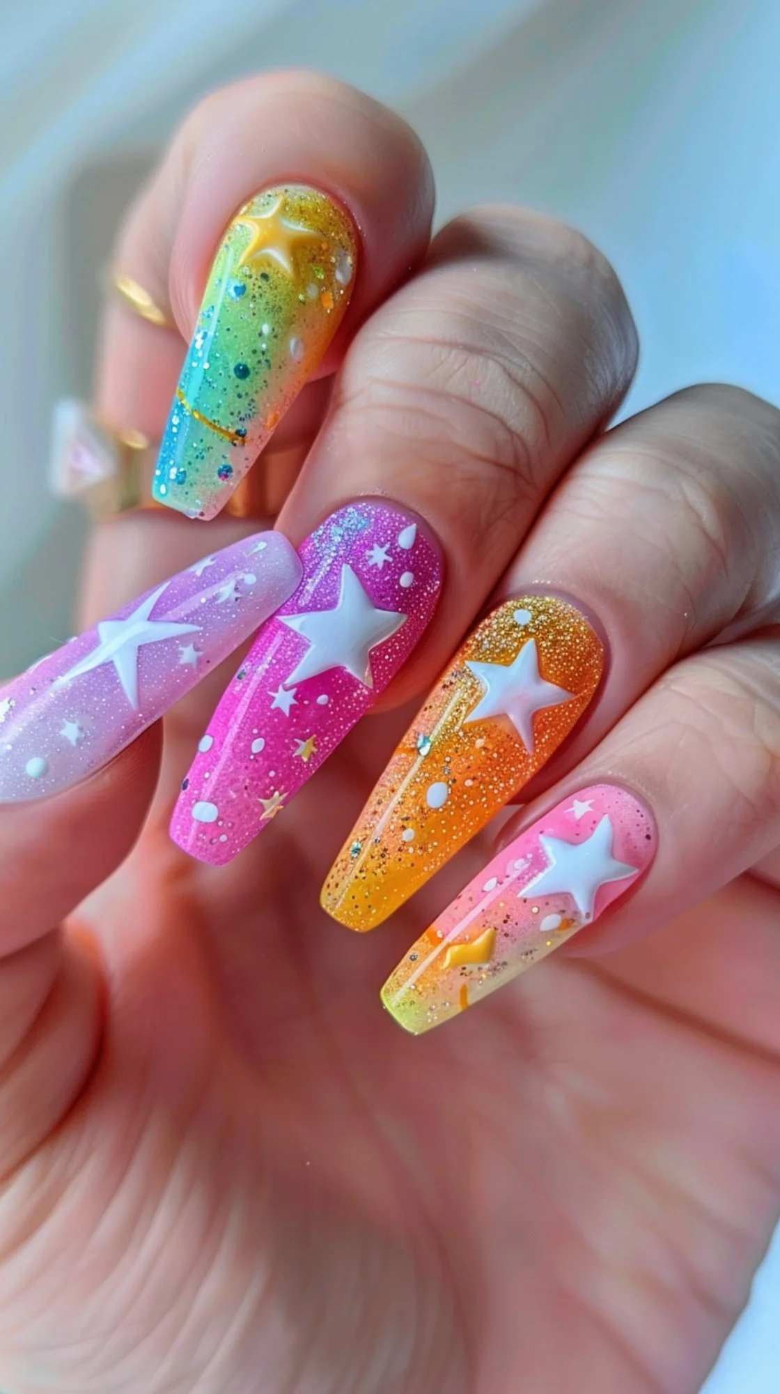 These long, almond-shaped nails are a vibrant festival of color with a gradient blending from a sunny yellow to a deep magenta, sprinkled with glitter and adorned with white star decals. The playful use of color and sparkle evokes the joy and whimsy of a summer carnival under a star-filled sky.