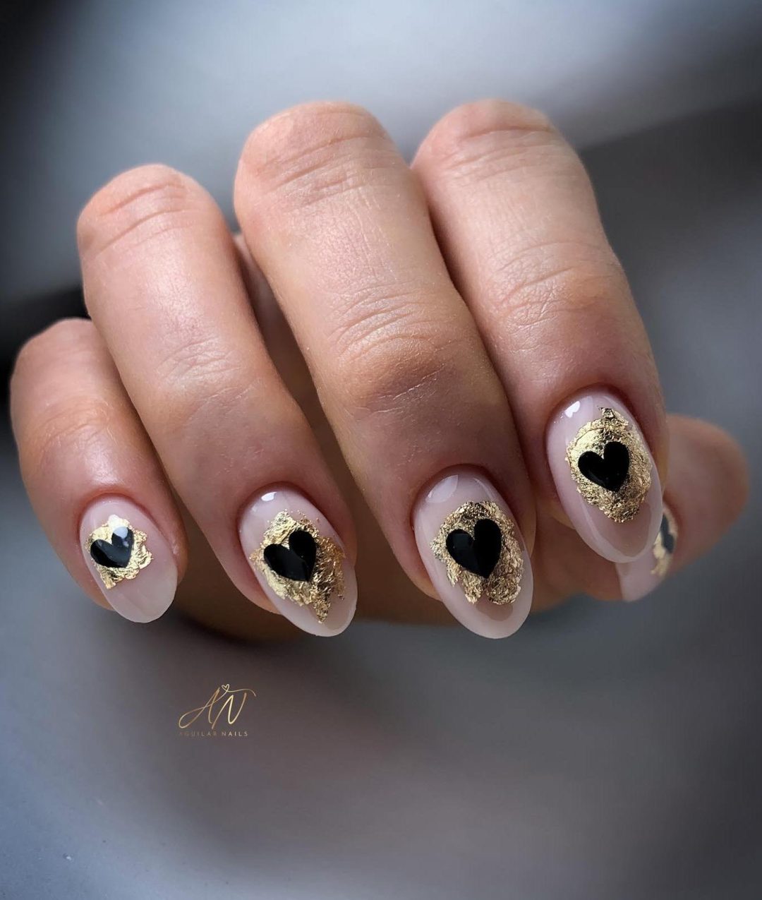 Neutral nails with gold foil and black hearts.