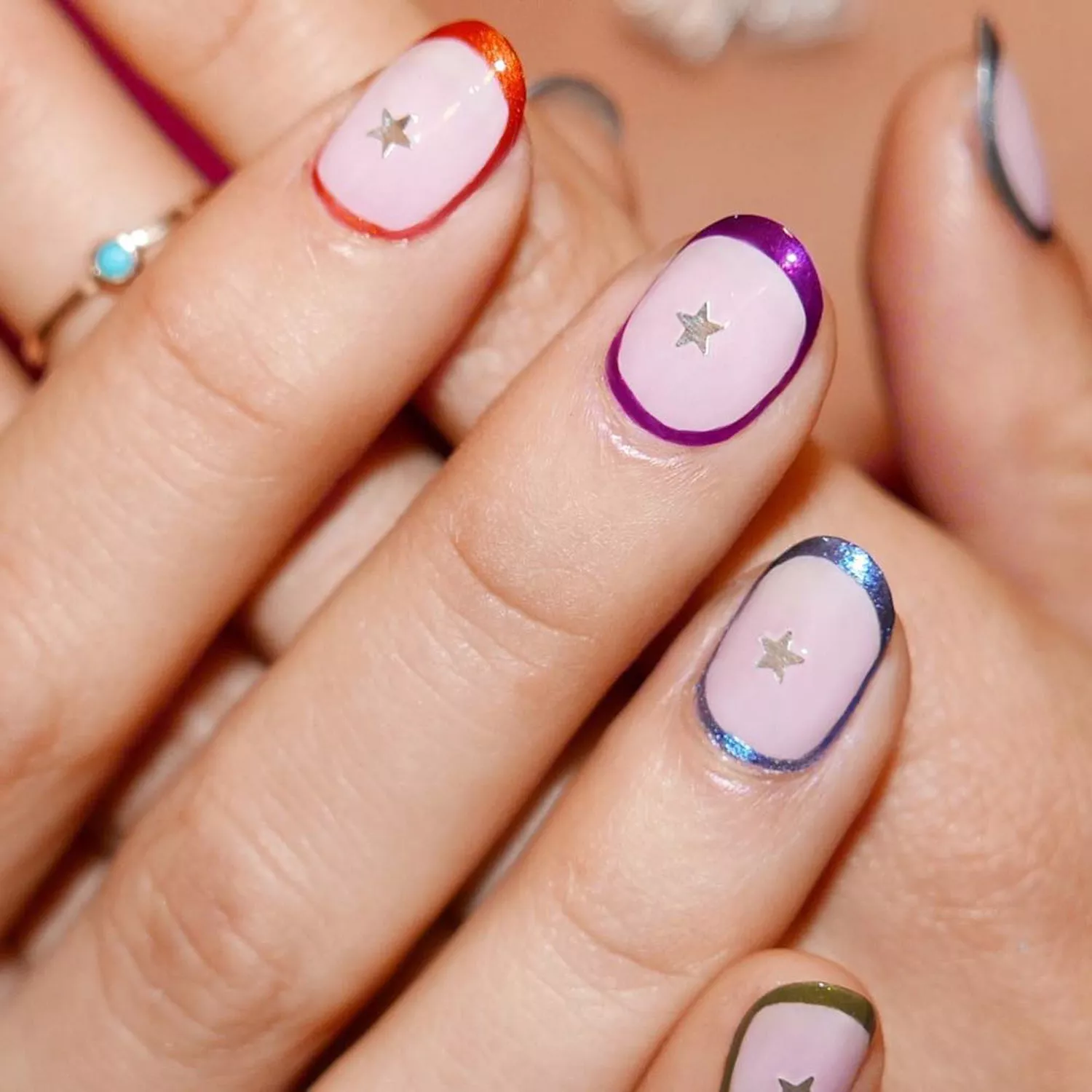 Hand with multi-colored chrome halos around each nail with silver star nair stickers at the center. 