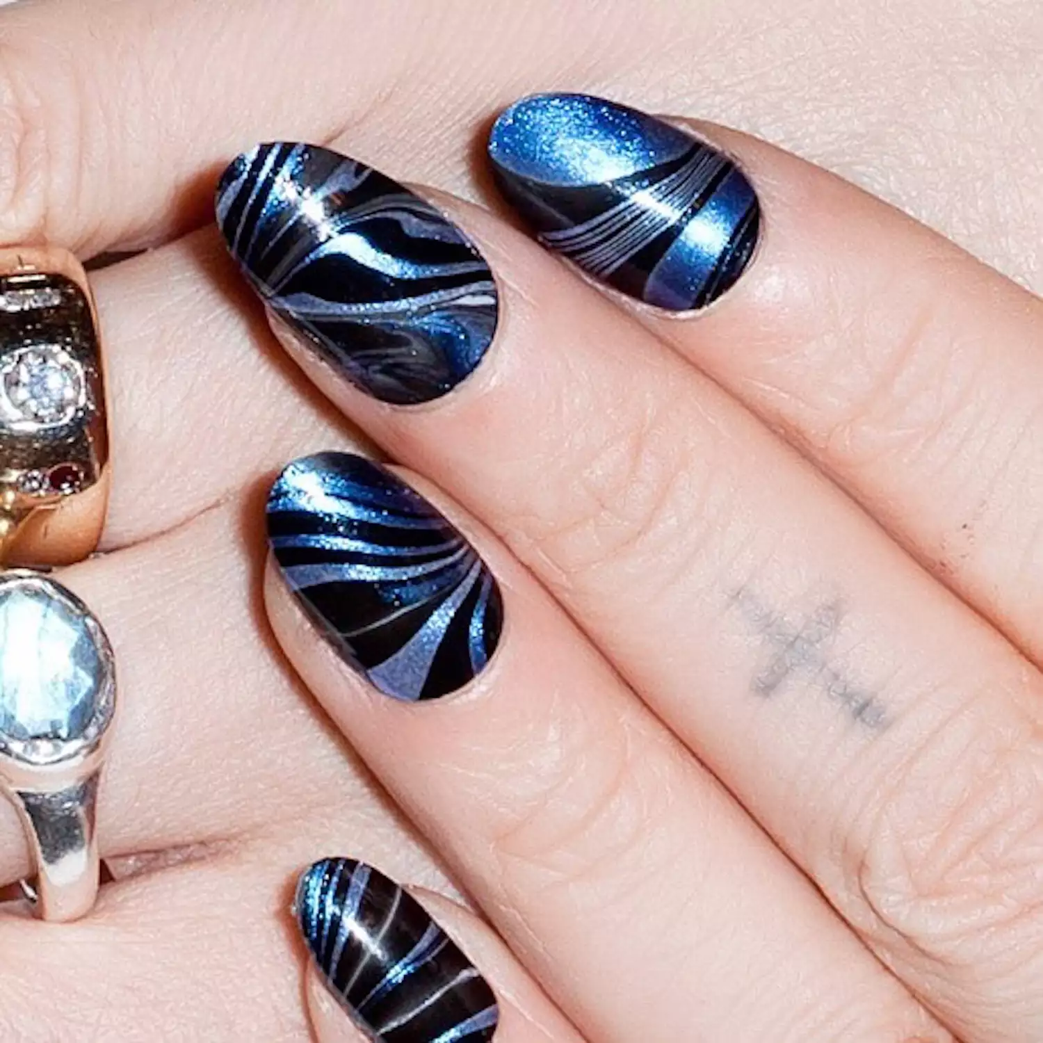 Hand with blue chrome marble pattern with black overlay on round nails.