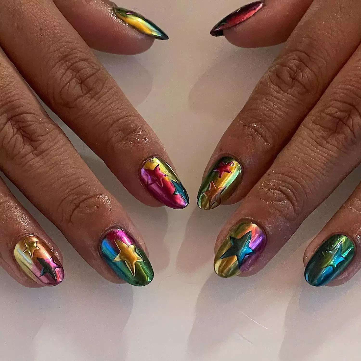 Hand with Rainbow chrome with 3D chrome stars scattered throughout the nails. 