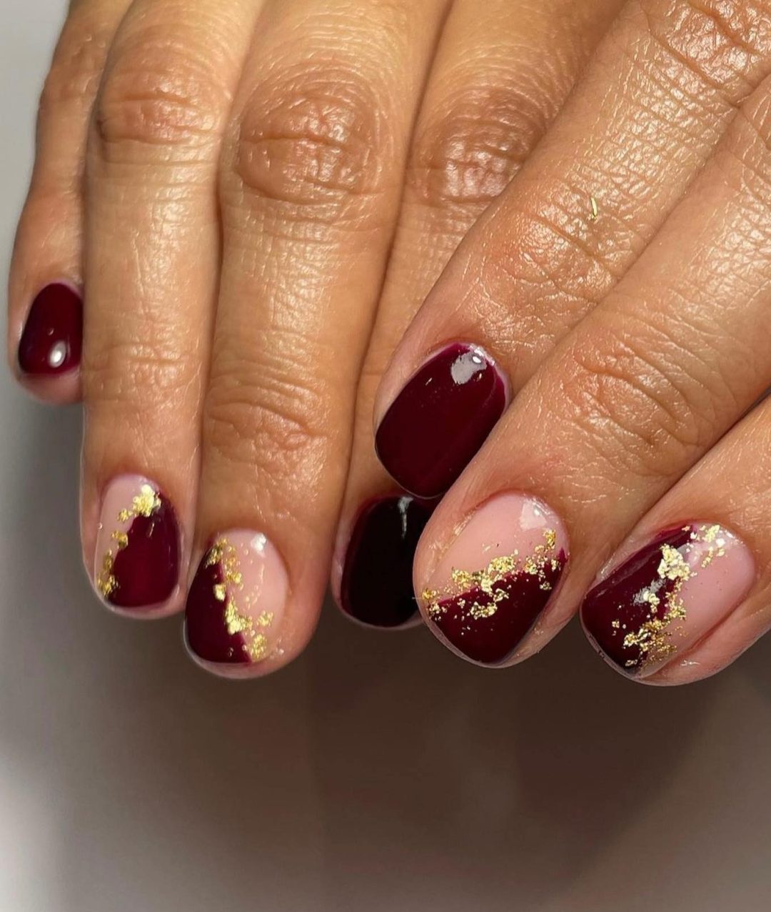 Short burgundy nails with gold foil.