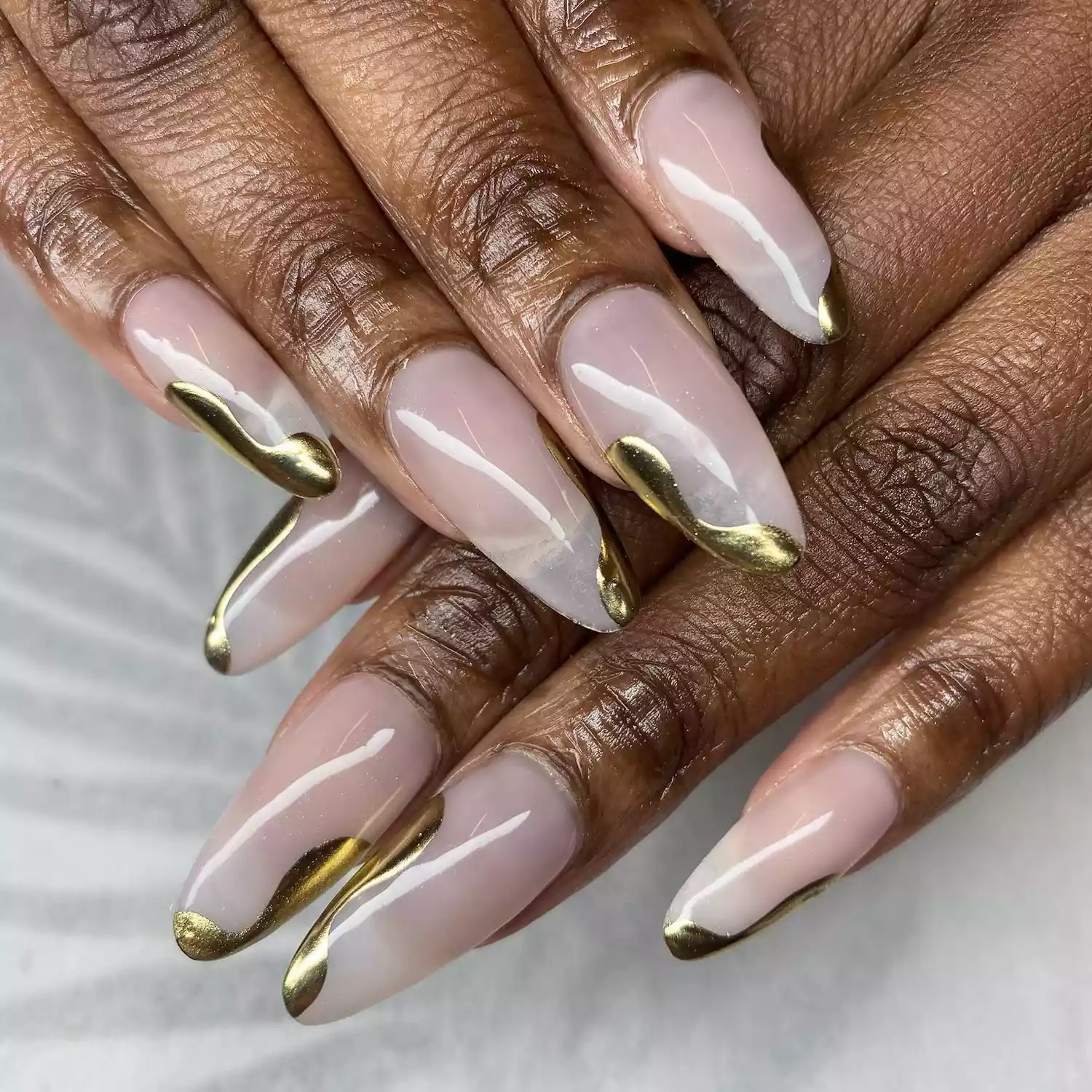 Hand with long almond shaped nails with gold chrome accents that look like drops of gold. 