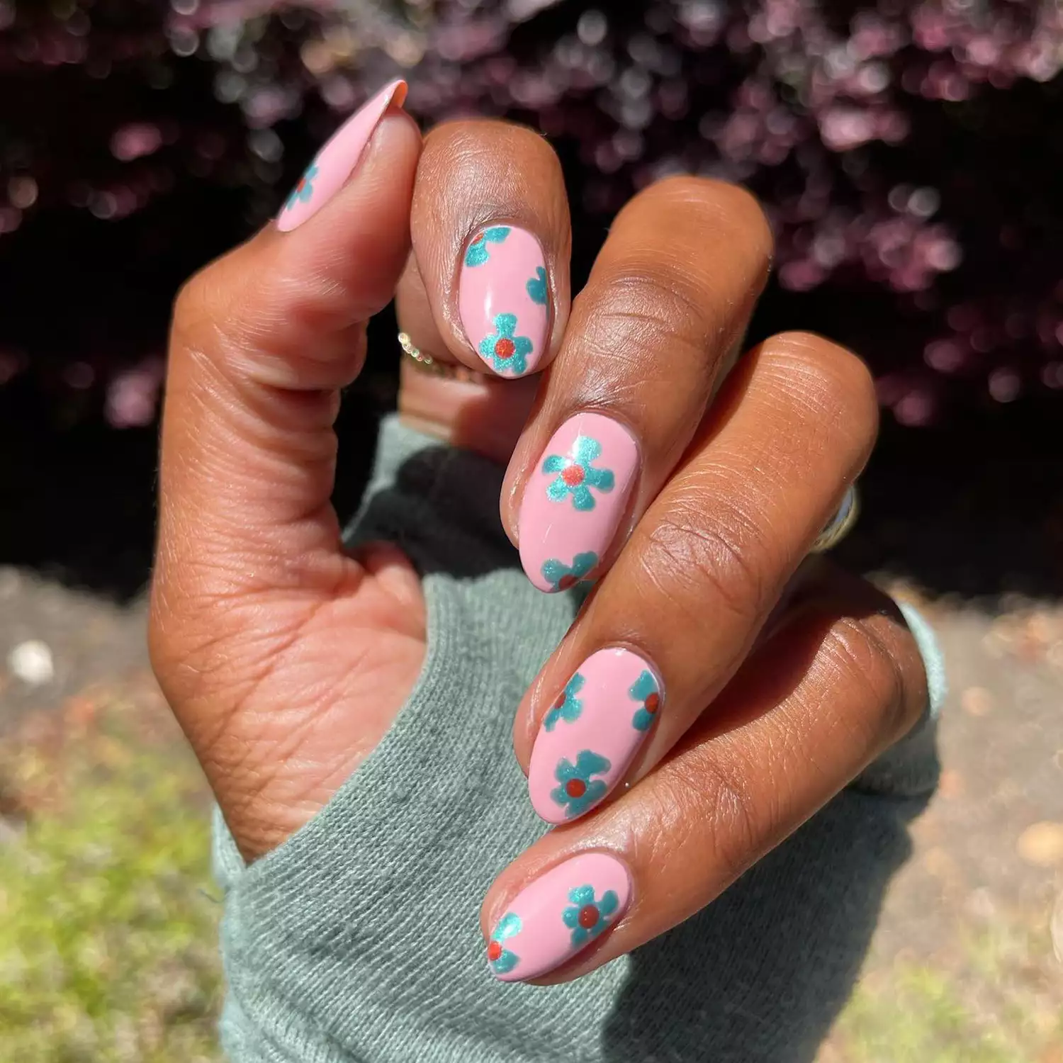 Hand with light pink polish with teal chrome flower nail art on each nail.